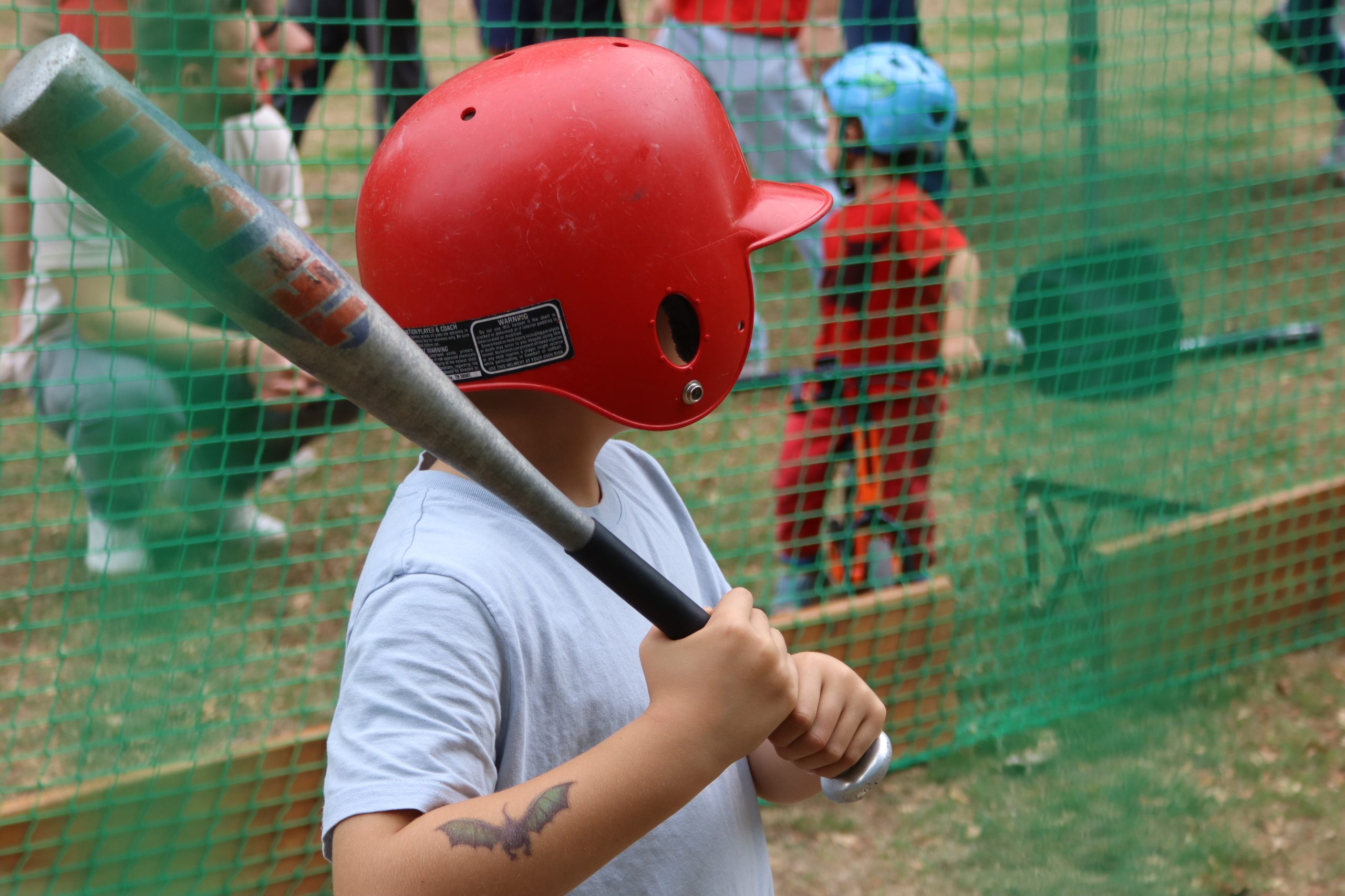 Kind mit Schlaghelm und Baseballschläger am Batting Cage
